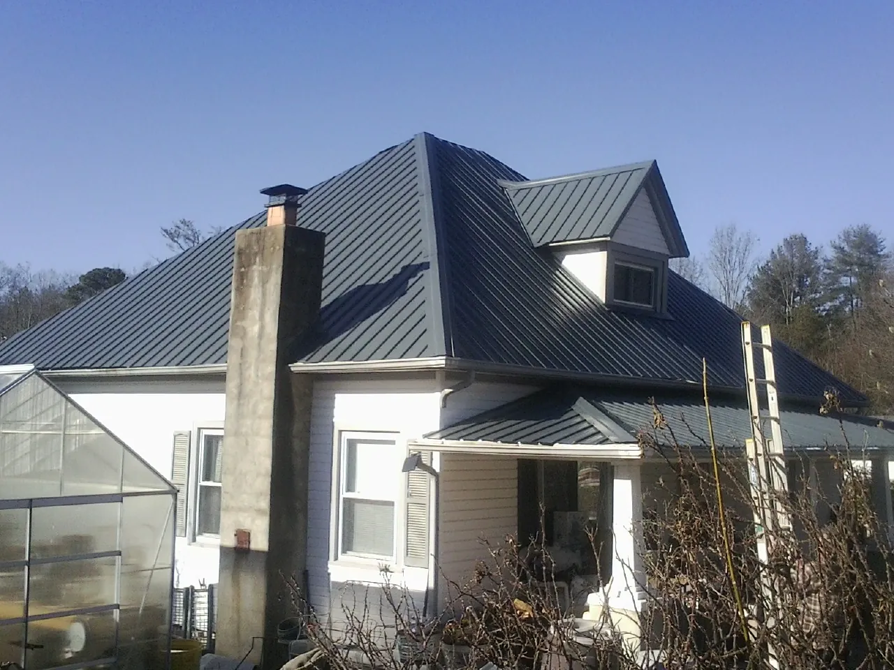 Dark blue standing seam metal roof on a white farmhouse with dormer — Slate & Tile Roof Repair by Roofing Brothers in Tonawanda