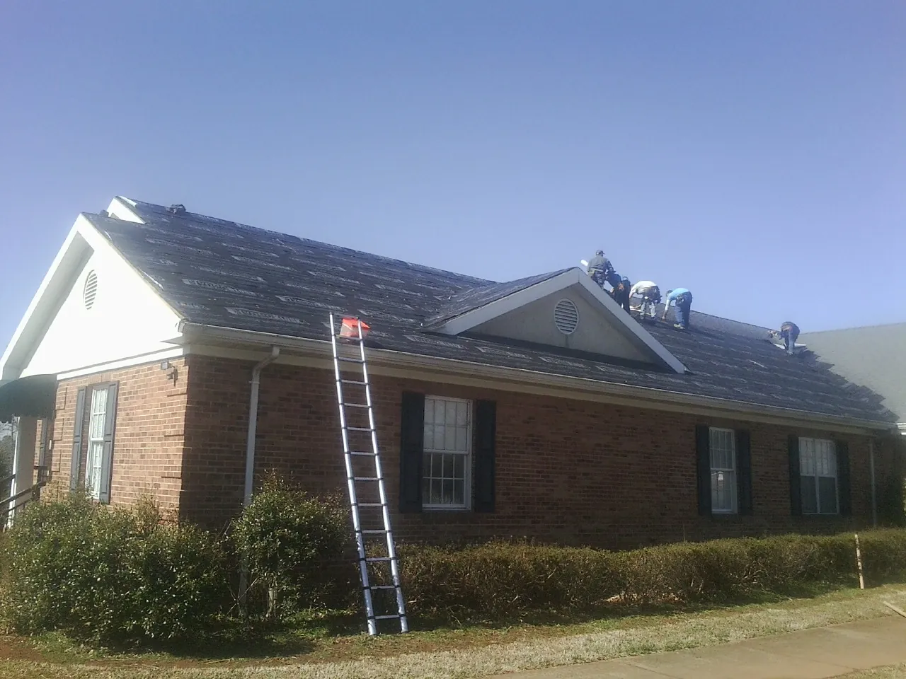 Crew tearing shingles off a brick ranch roof with a ladder set — Emergency Roof Repair work by our crew in Tonawanda