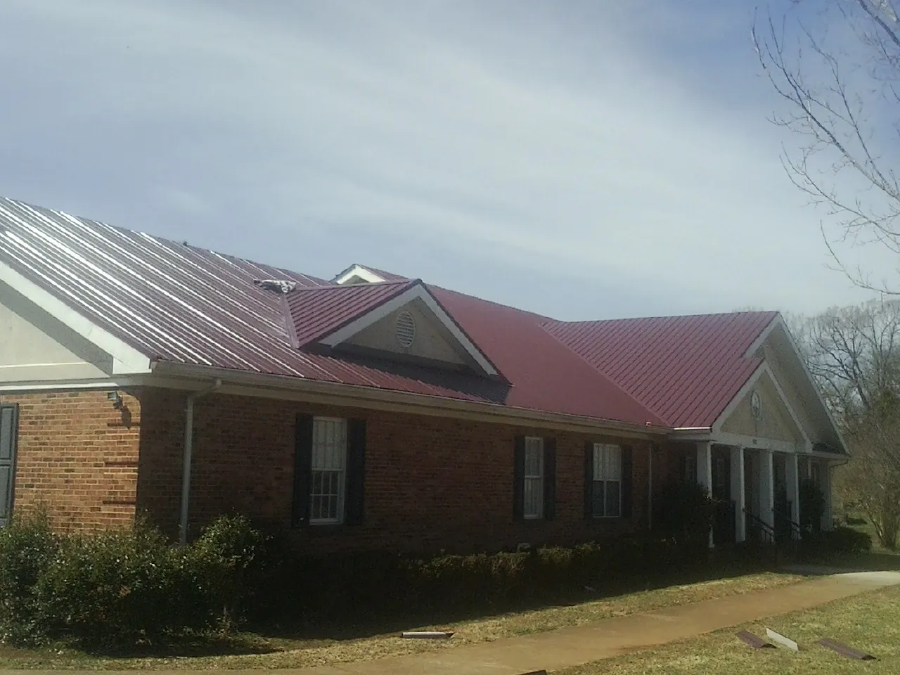 Red metal roof with gabled entries on a long brick building, from a Hail Damage Roof Repair job in Tonawanda