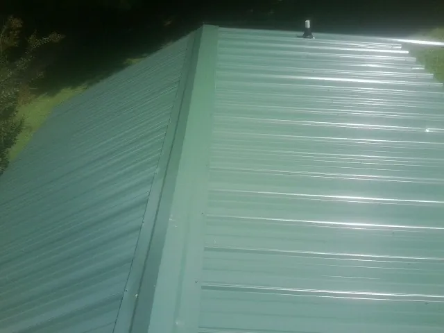New green metal panels meeting at the ridge of a roof — Flat Roof Repair work by our crew in Tonawanda