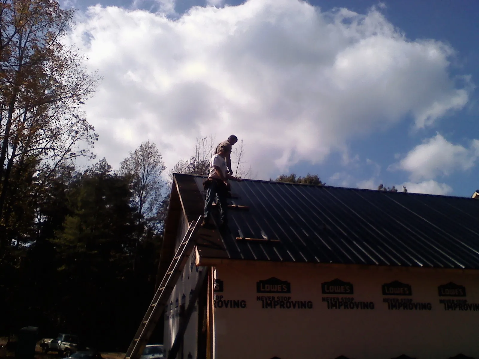 Roofer fastening dark metal panels high against a cloudy sky, from a Roof Inspection job in Tonawanda