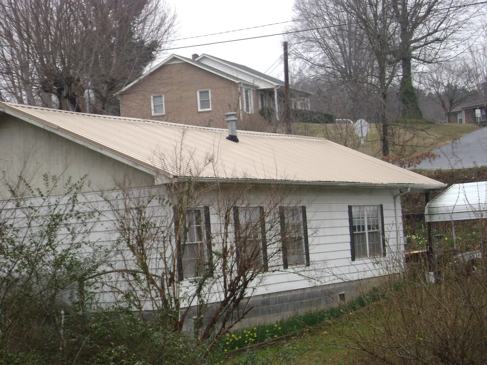 Tan metal roof on a white sided house set into a hillside — Commercial Roofing by Roofing Brothers in Tonawanda
