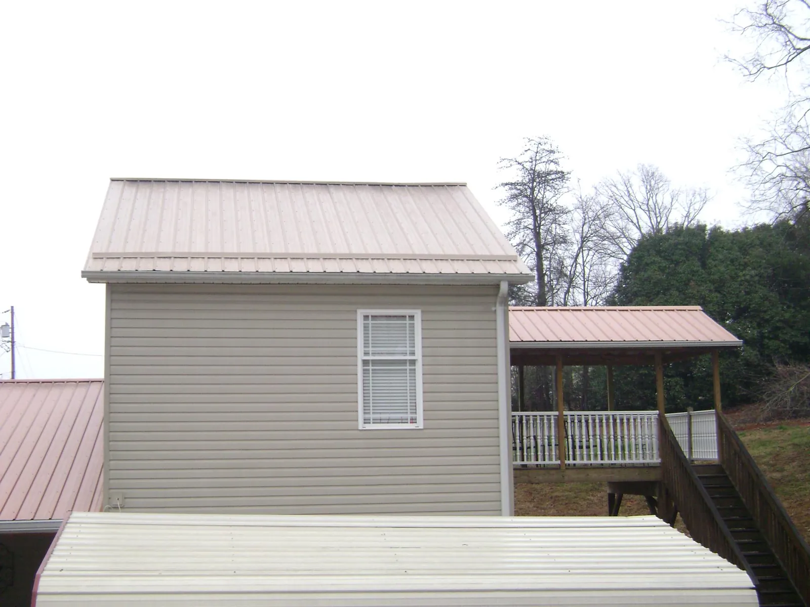 Tan metal roofs on a two story addition and attached porch, from a Roof Replacement job in Tonawanda